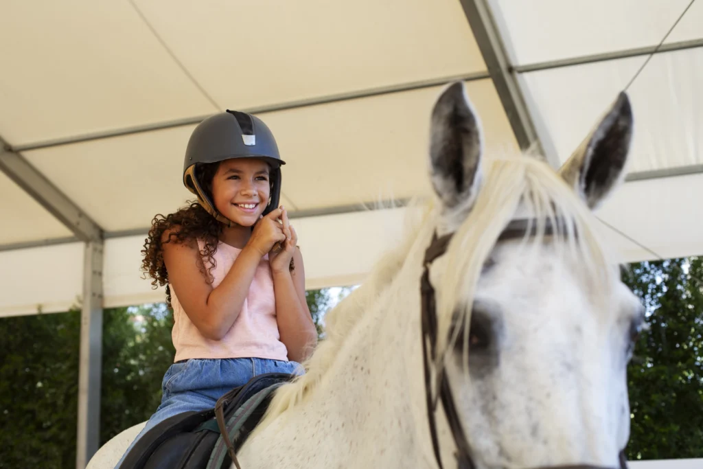 Ragazzina che indossa il cap da equitazione durante una lezione, attrezzatura personale che accompagna la crescita nel tempo