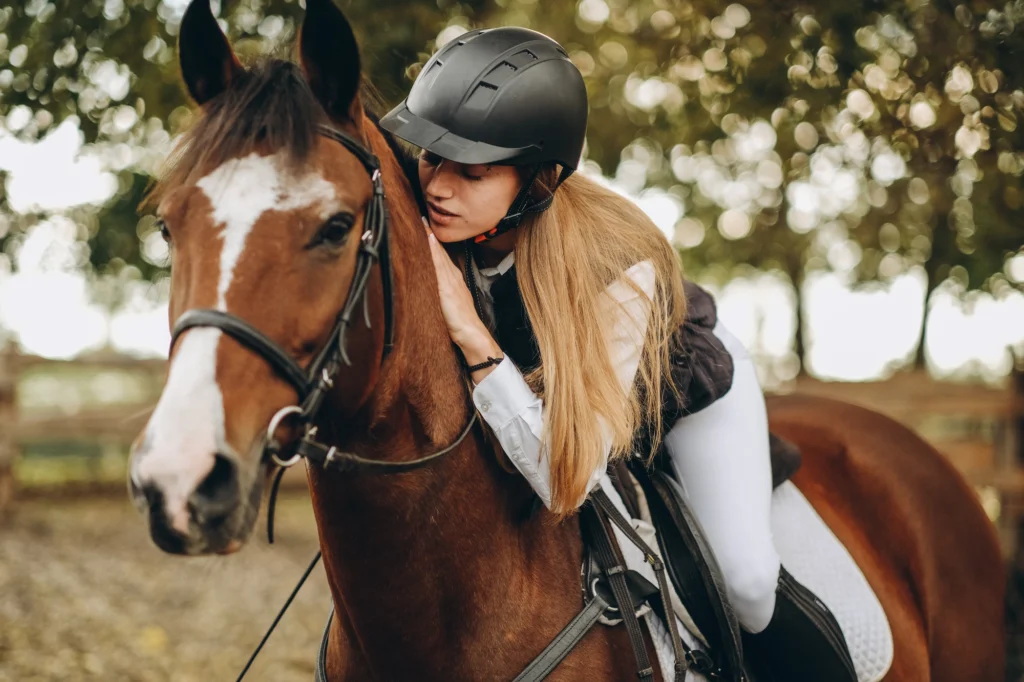 Ragazza a cavallo che abbraccia il proprio cavallo durante un momento di connessione emotiva nel maneggio